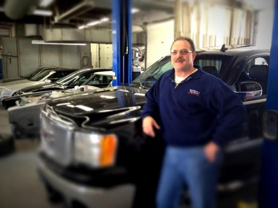 A man with a mustache is standing next to a truck in a garage
