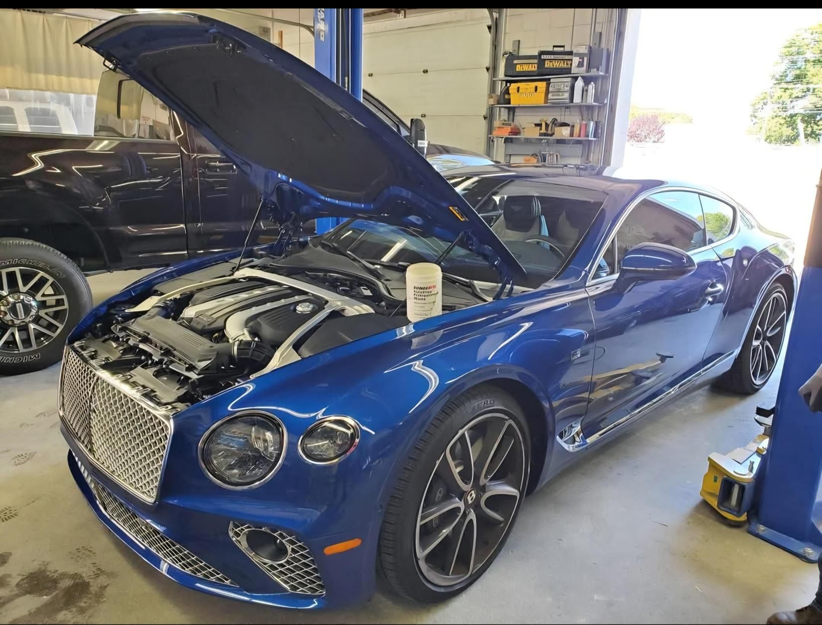 A blue Bentley is parked in a garage with the hood up.