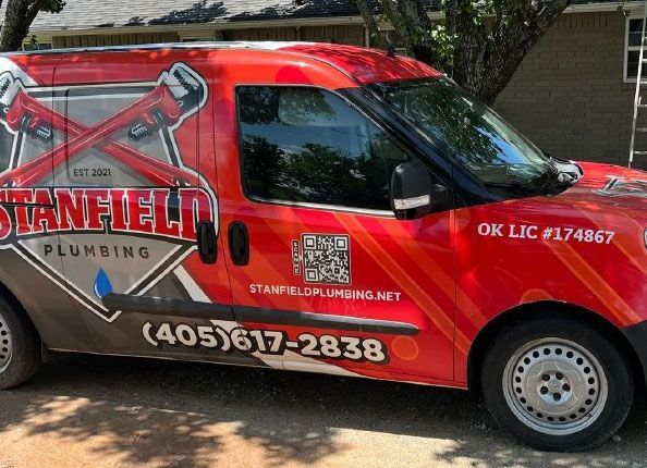 Red Stanfield Plumbing van with logo, phone number, and ladder graphic parked outdoors