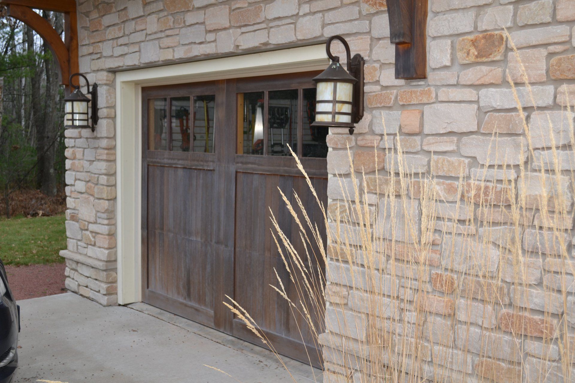 A car is parked in front of a wooden garage door on a brick building.