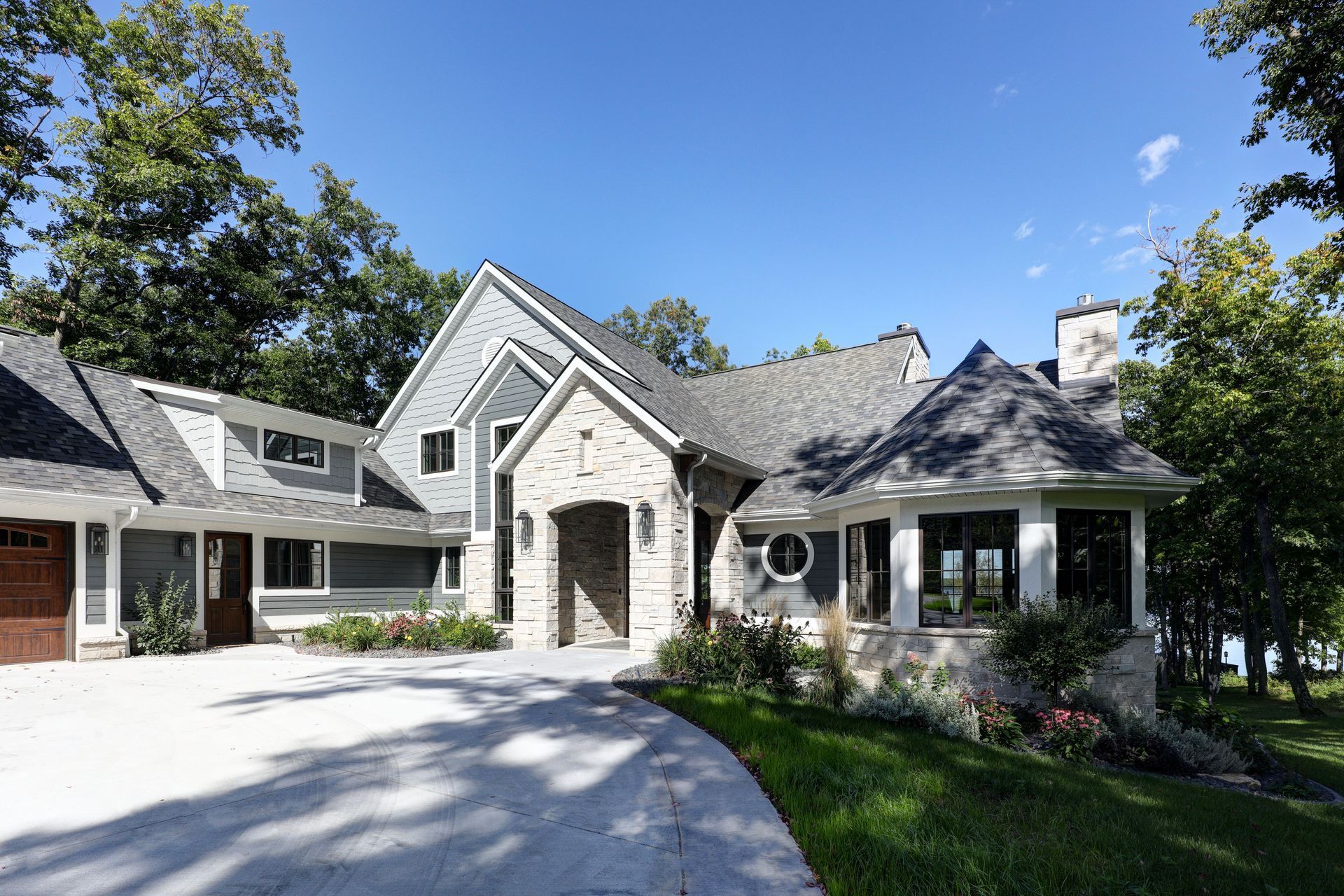 House with gray and stone exterior, driveway, trees, and blue sky.