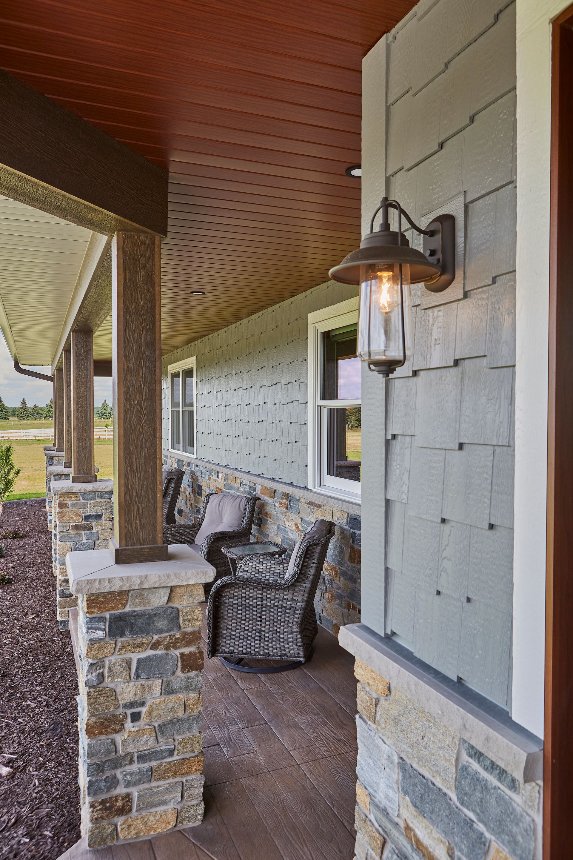A porch with chairs and a lamp on the side of a house
