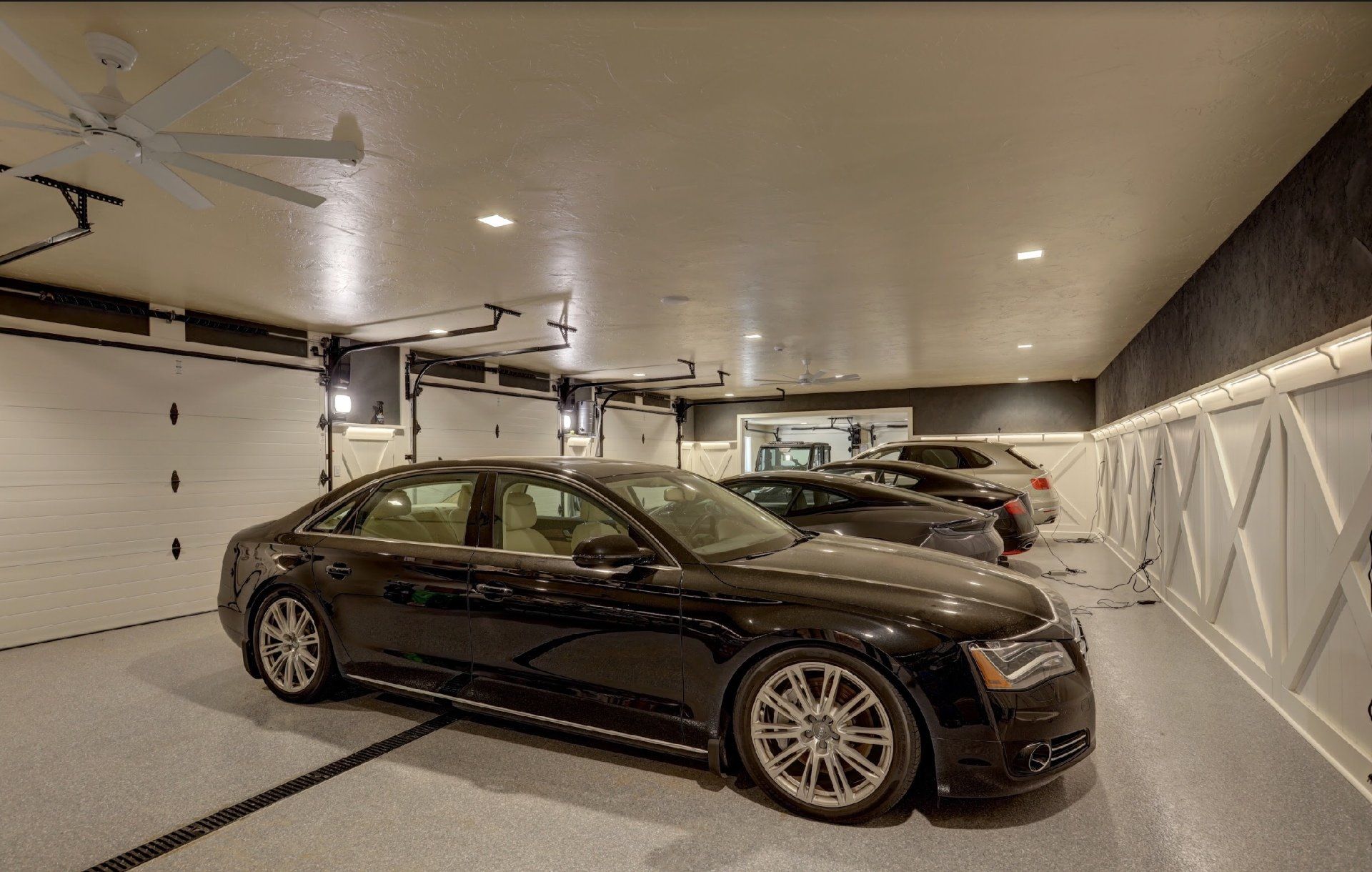 A black car is parked in a garage with other cars.
