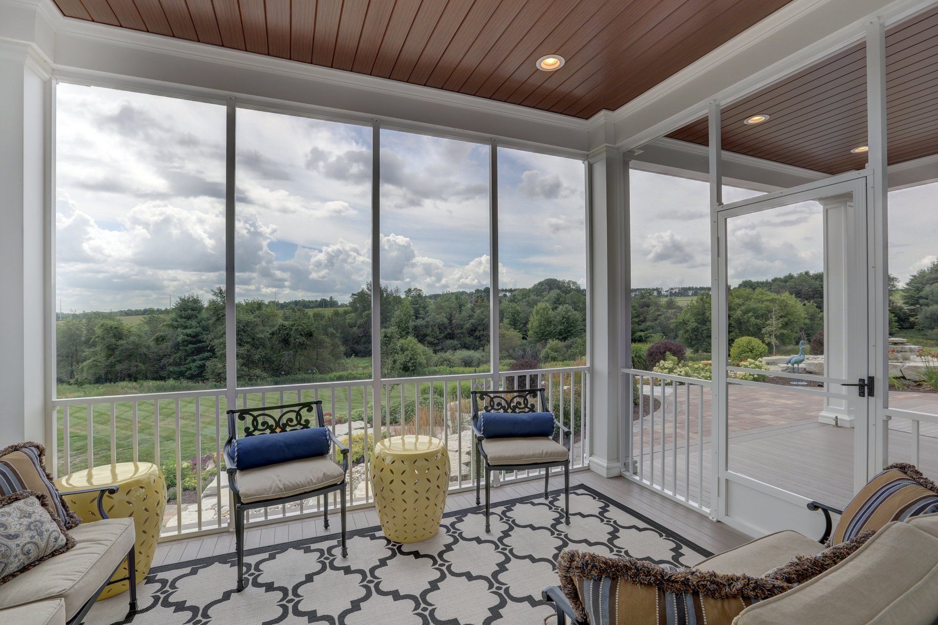 A screened in porch with a lot of windows and chairs.