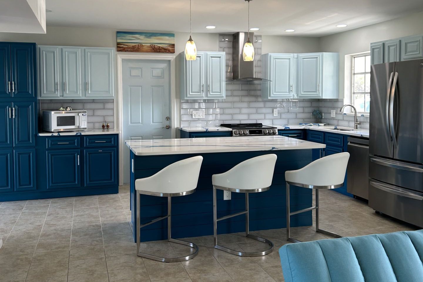 A kitchen with blue cabinets and white stools and a blue couch.