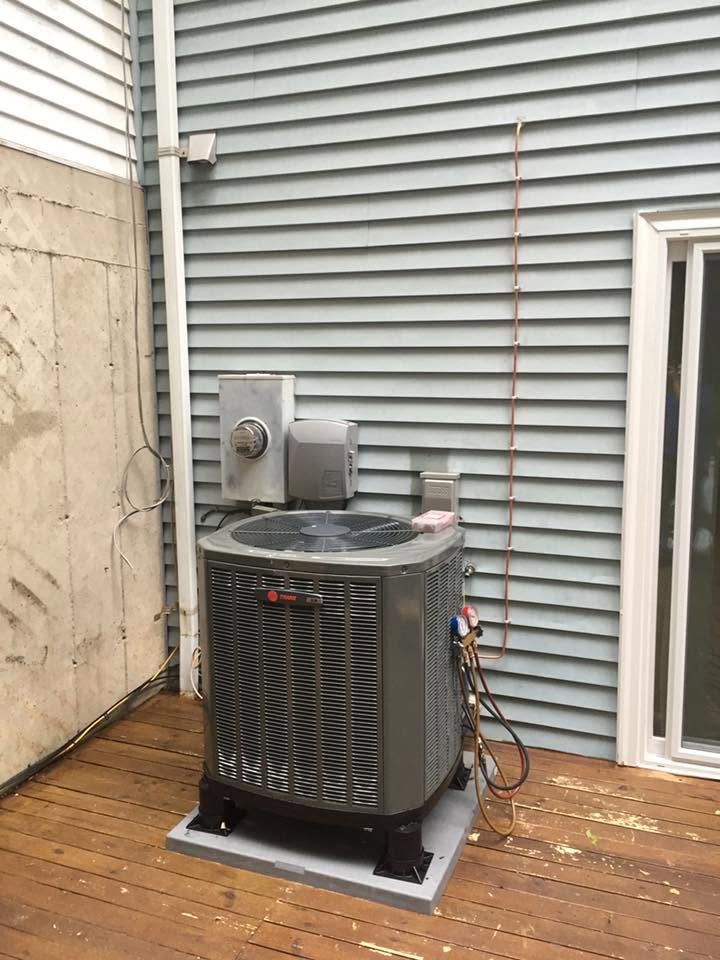 Outdoor air conditioner unit on a concrete pad beside a house, with a grill and siding in the background