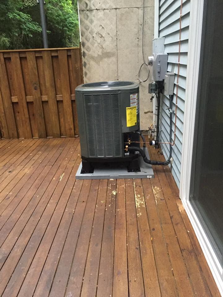 Backyard wooden deck with an air conditioner unit beside a house wall and fence.