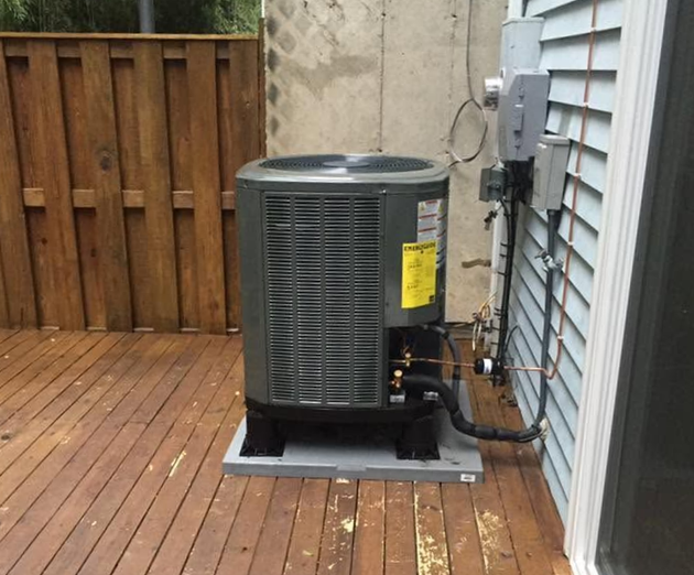 Air conditioner unit on a wooden deck beside a house and fence