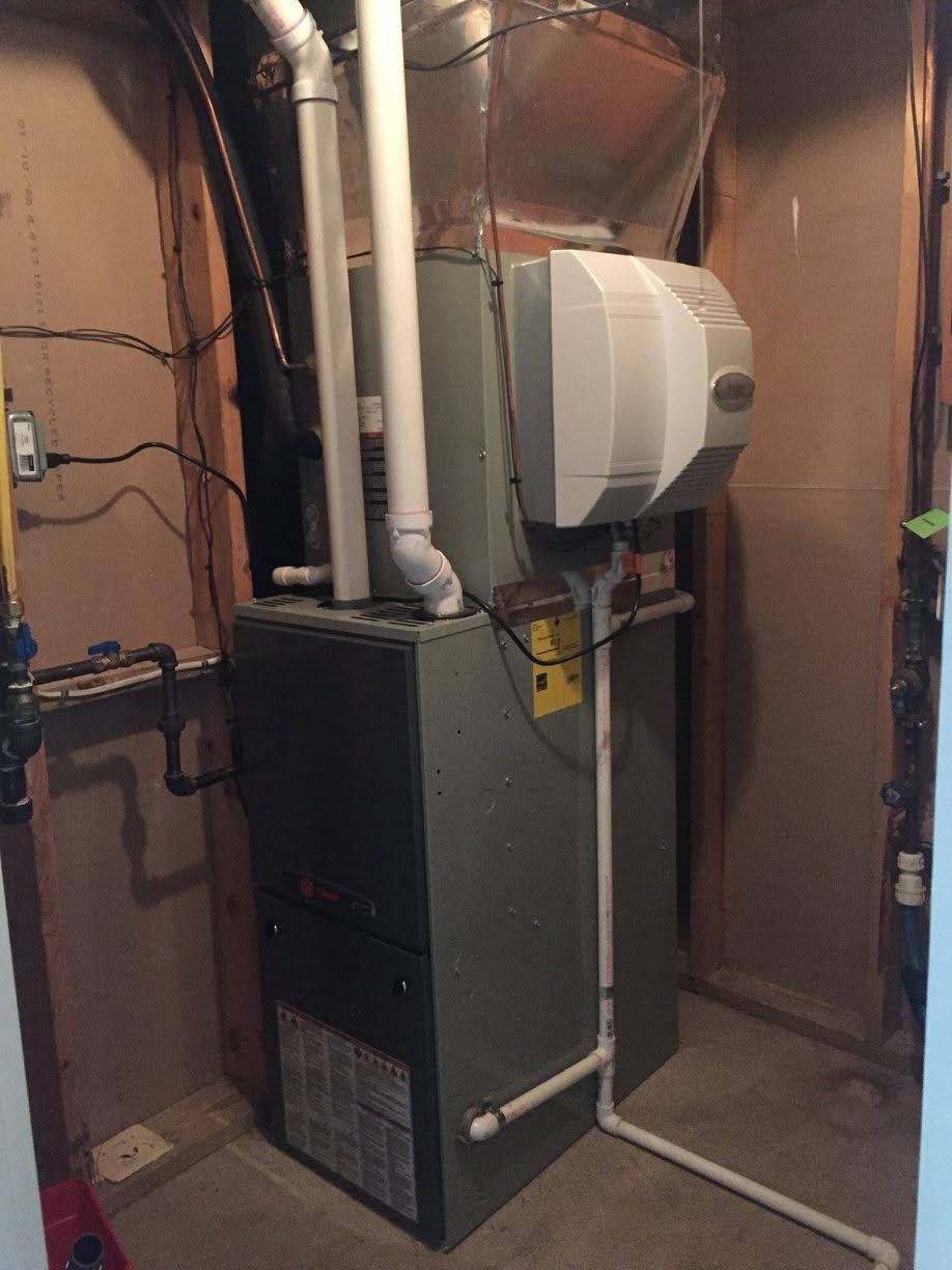 Furnace and HVAC ductwork in a cramped utility closet with exposed pipes and wiring.