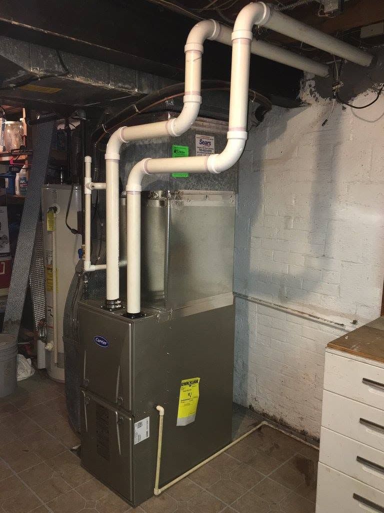 Basement furnace with white PVC pipes and black unit against concrete wall, utility room setting