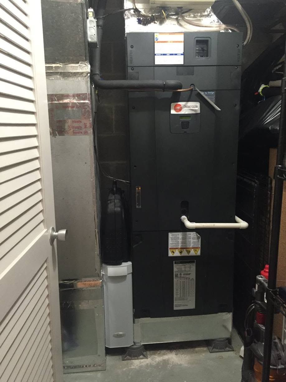 HVAC furnace unit in a narrow utility closet with exposed ductwork and piping