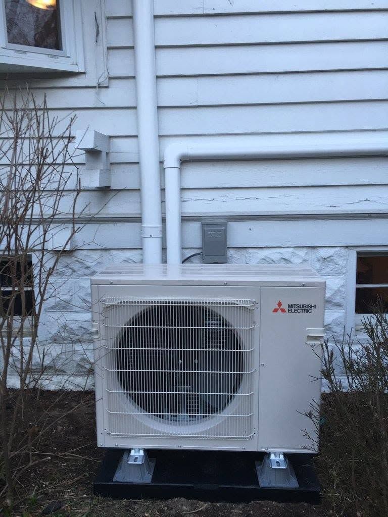 Outdoor Mitsubishi mini-split AC unit beside a house wall and window, with pipes running into the siding