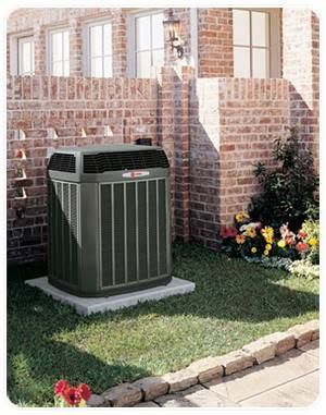 Outdoor air conditioner unit beside a brick house and flower bed
