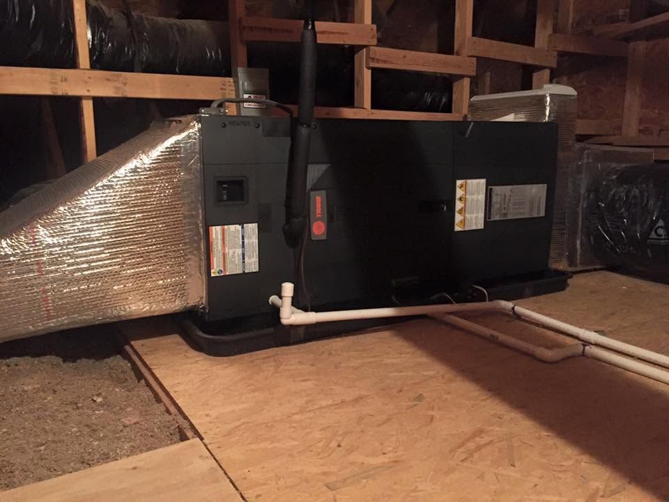 Furnace and HVAC ductwork in an attic, with insulated silver venting and black unit on a plywood floor.