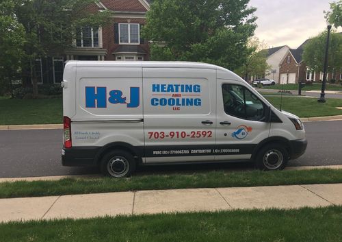 White H&J Heating & Cooling van parked on a suburban street in front of houses.