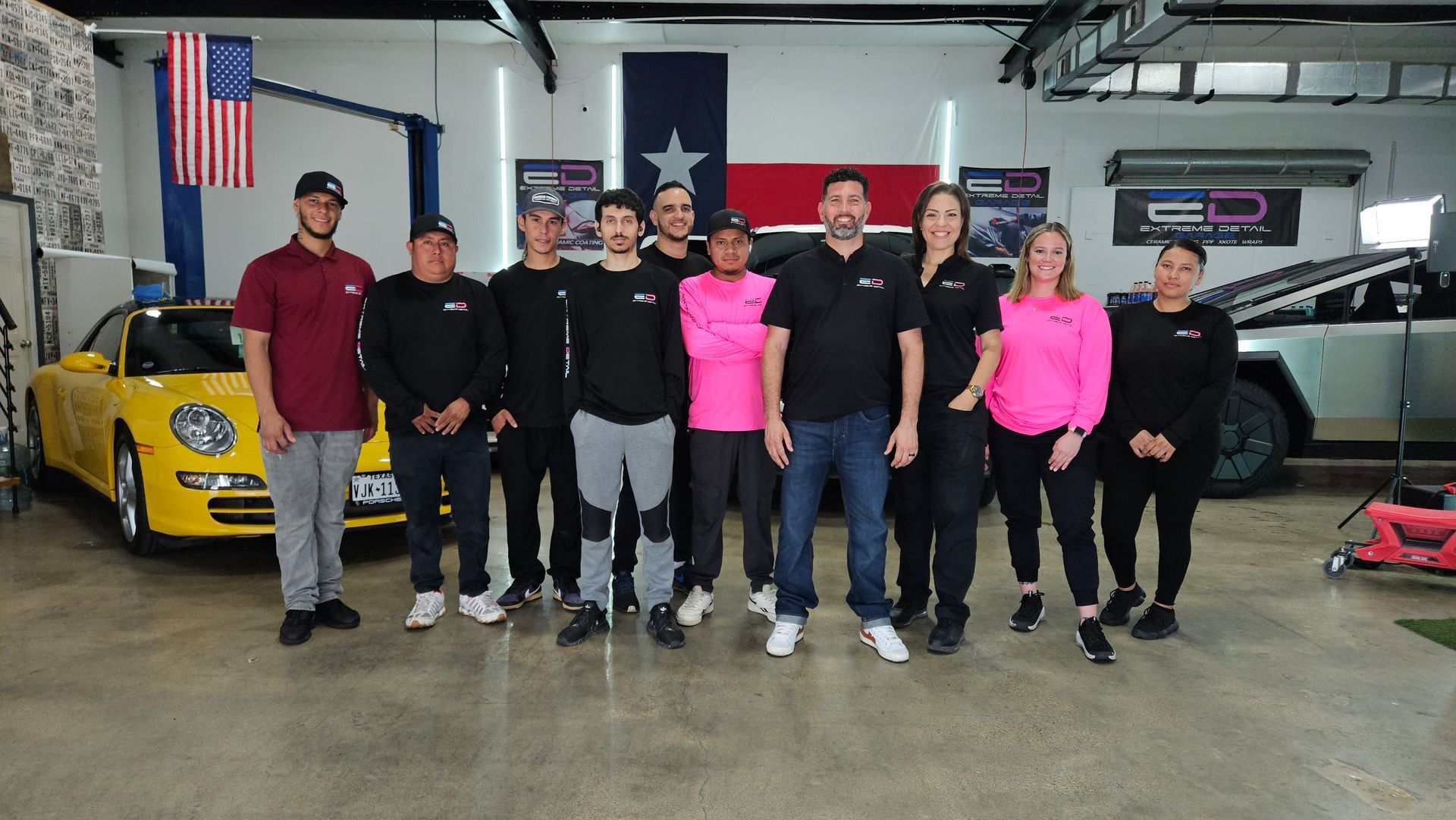 A group of people standing in front of a yellow car in a garage.