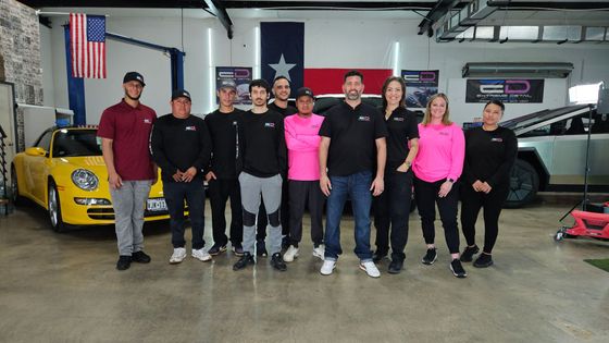 A group of people standing in front of a yellow car in a garage.