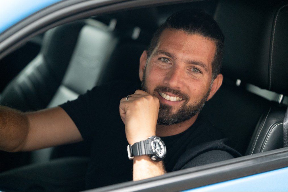 A man with a beard is sitting in the driver 's seat of a car.