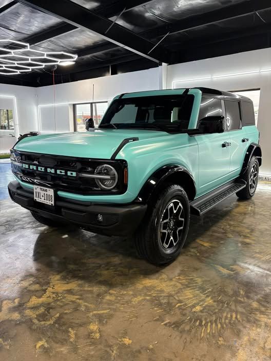 Mint green Ford Bronco SUV parked indoors in a showroom, black roof and wheels.