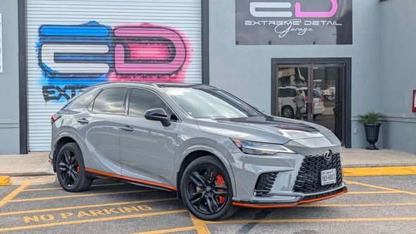 Gray sporty SUV parked outside a tuning shop with neon pink and blue wall art