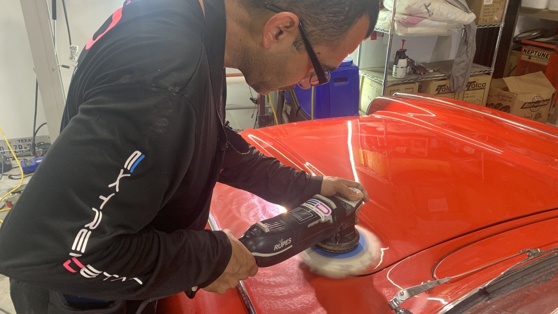 A man is polishing a red car with a machine.