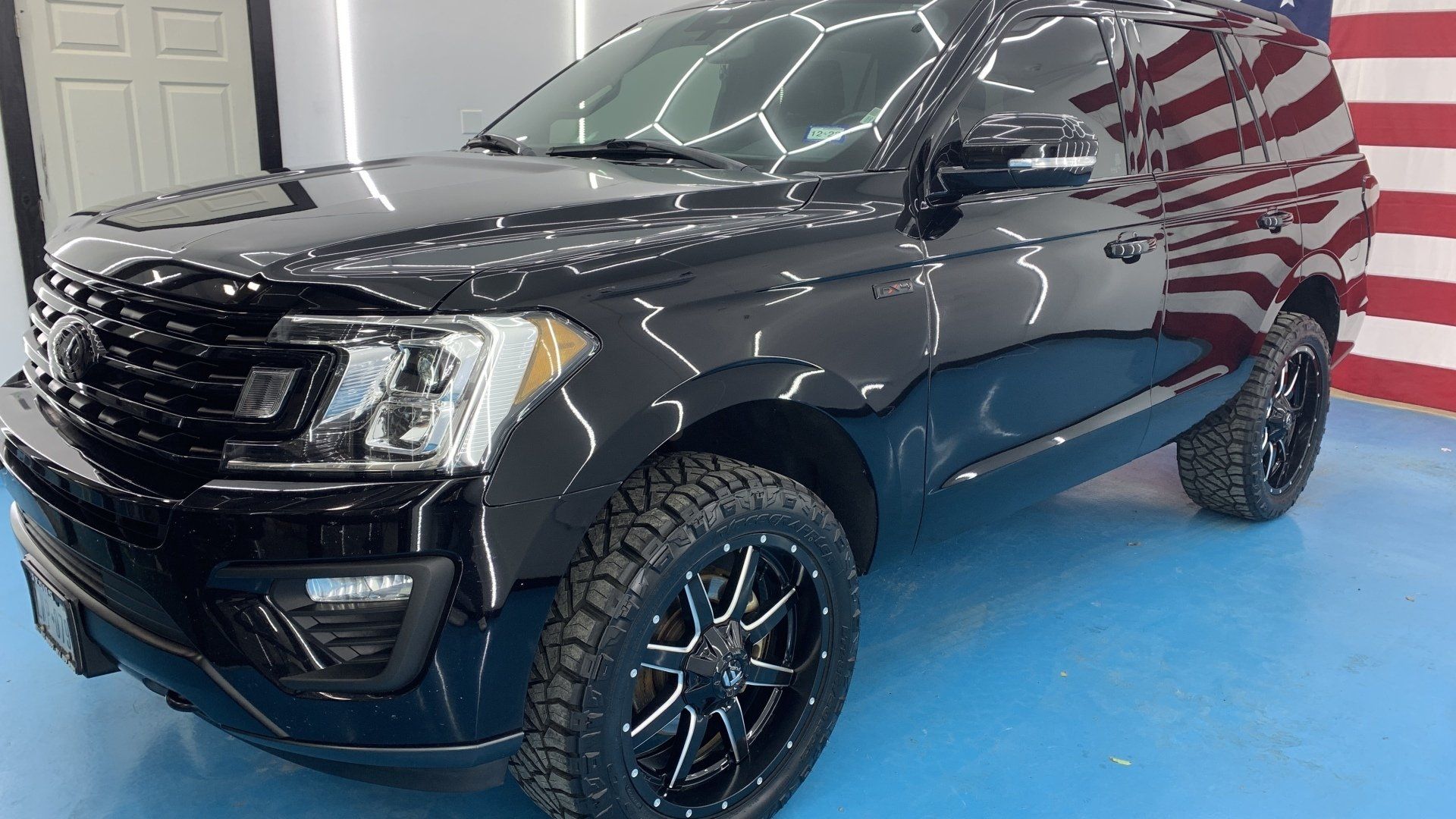 A black ford expedition is parked in front of an american flag.