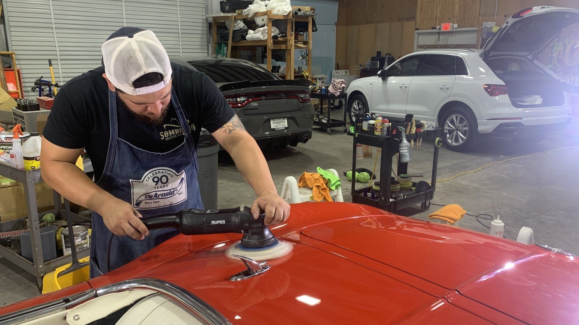 A man is polishing a red car in a garage.