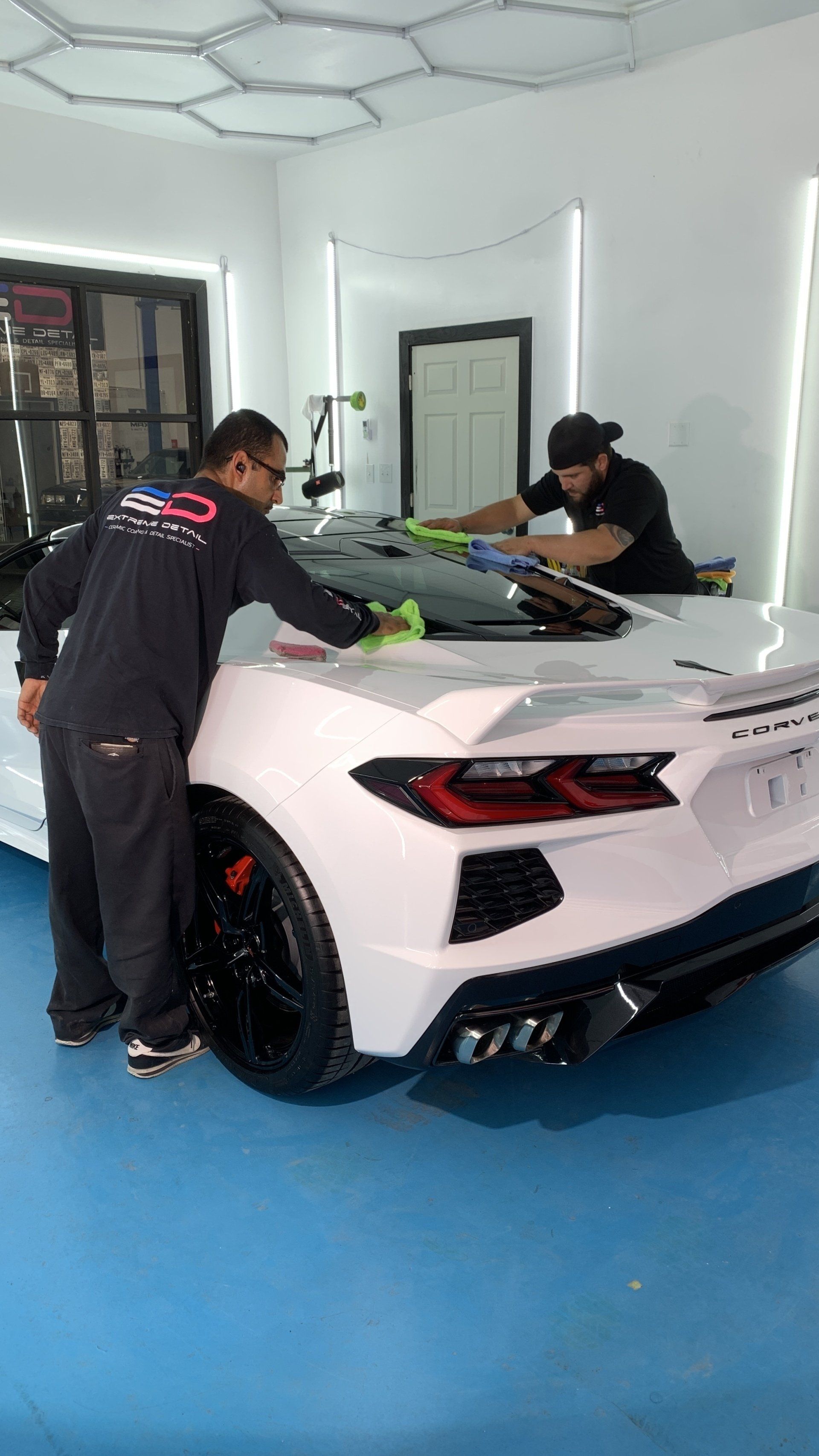 Two men are working on a white sports car in a garage.