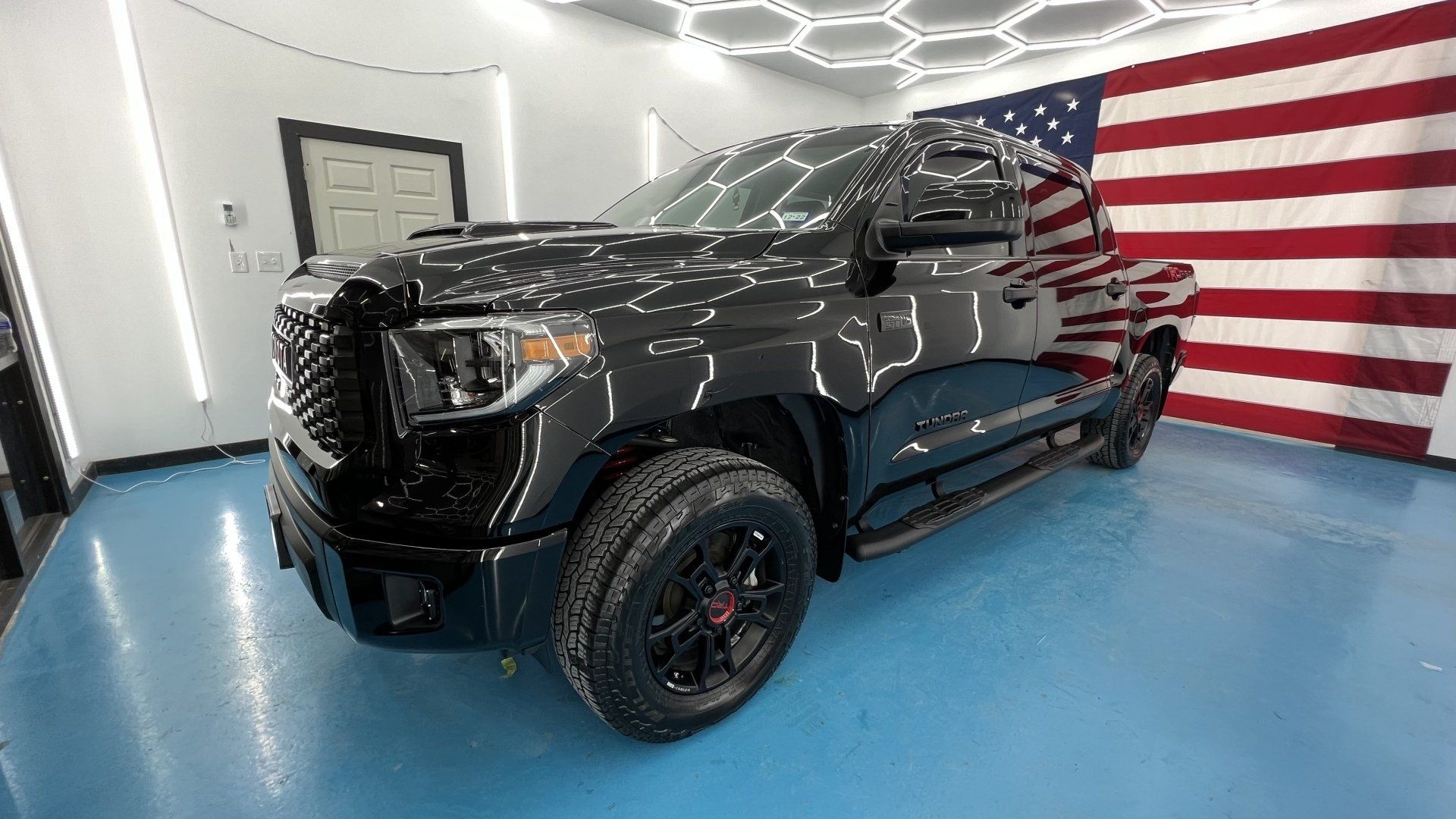 A black truck is parked in a garage next to an american flag.