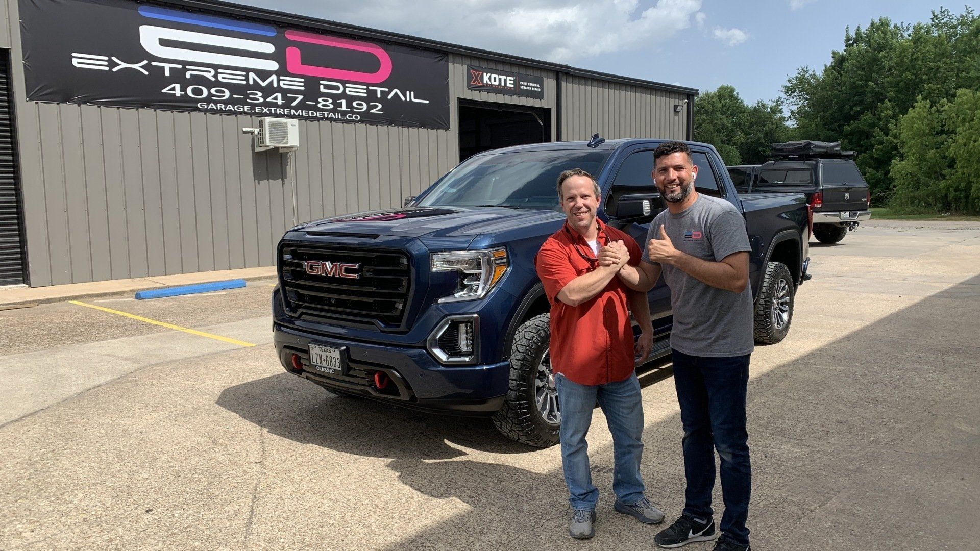 Two men are standing in front of a gmc truck.