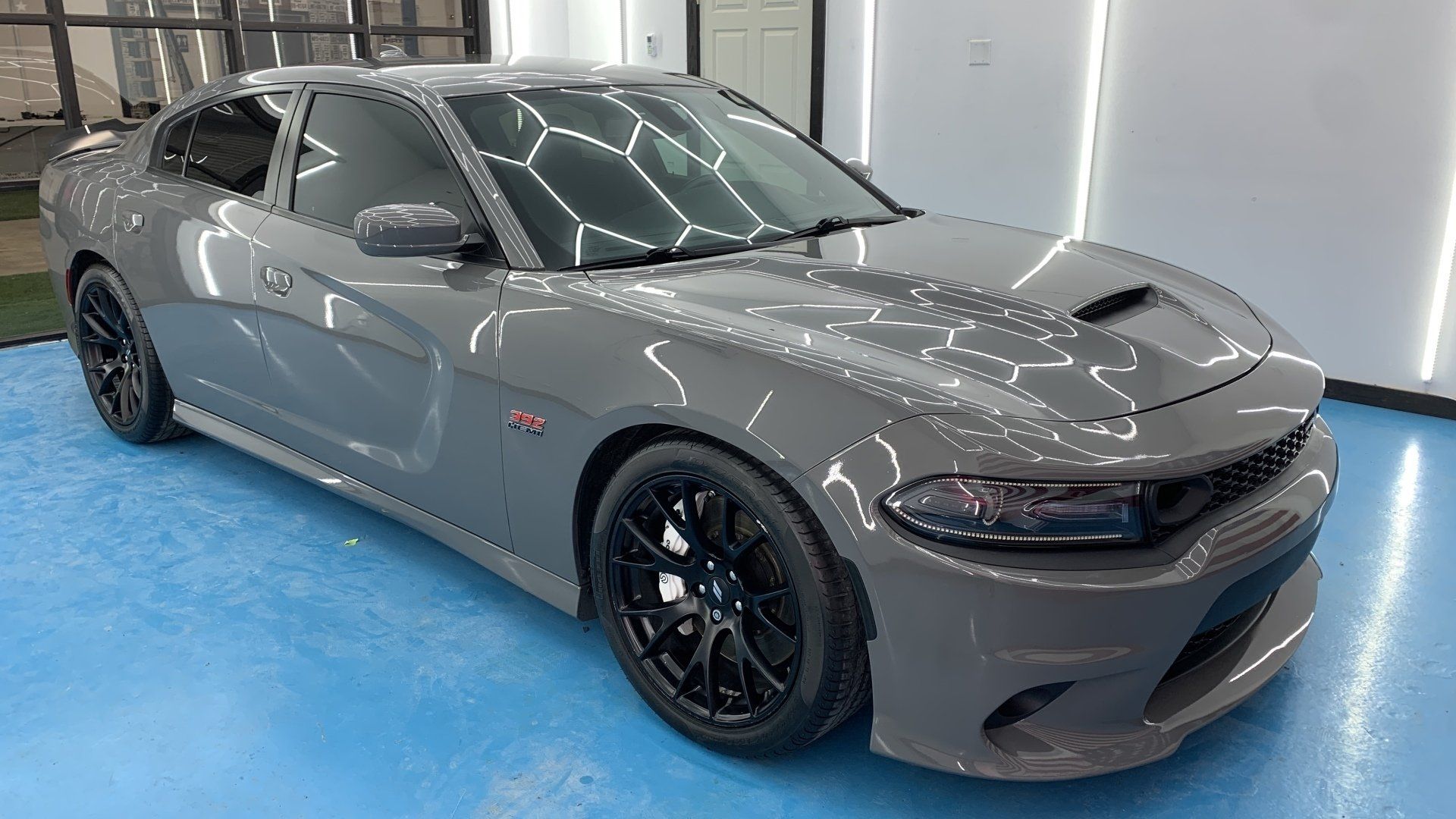 A gray dodge charger is parked on a blue floor in a garage.
