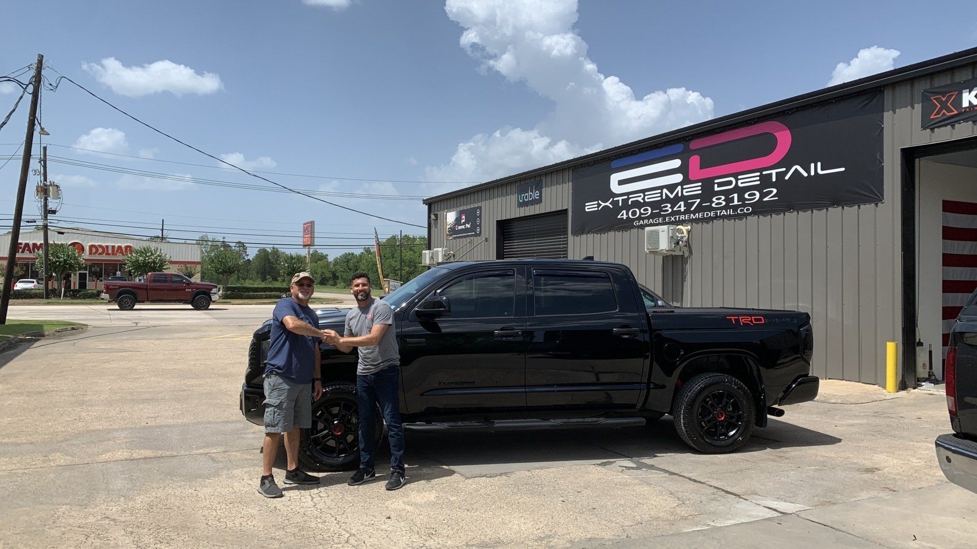 Two men are shaking hands in front of a truck in a parking lot.