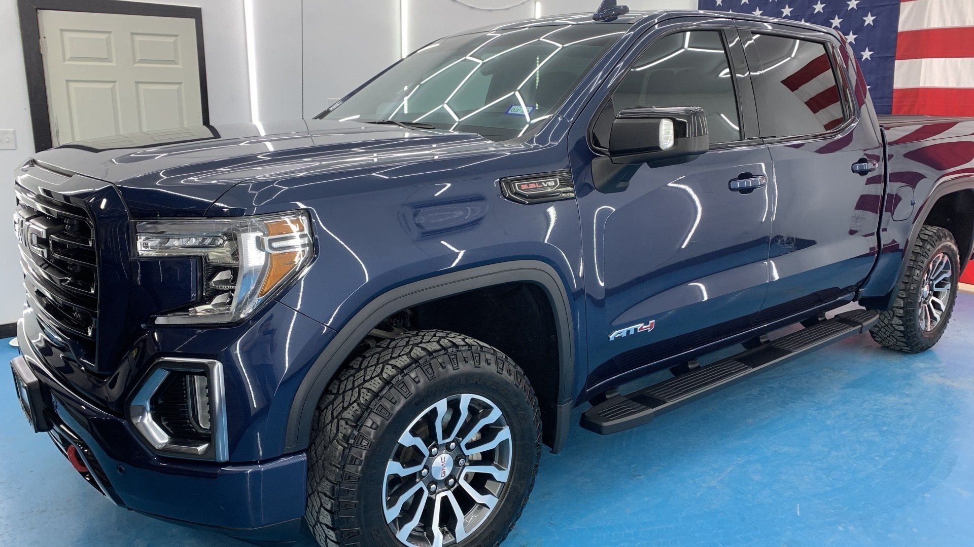 A blue pickup truck is parked in front of an american flag.