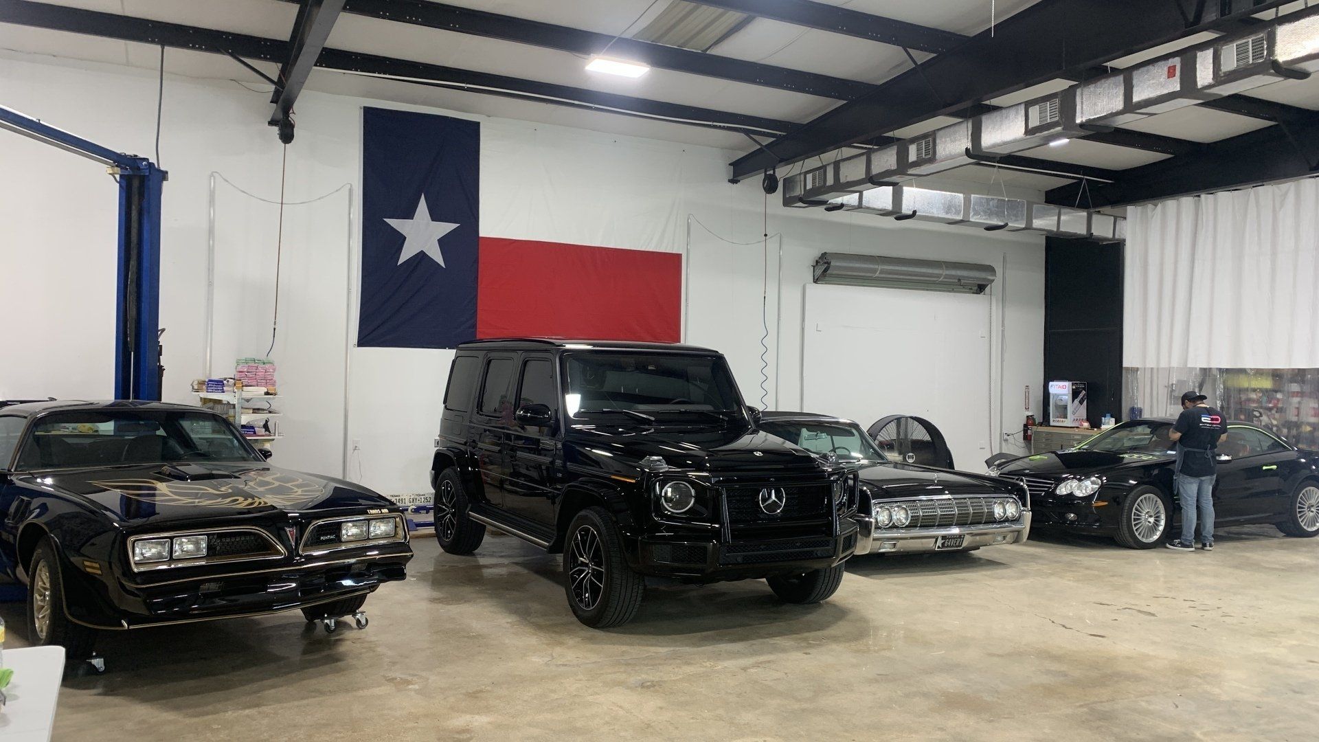 A row of cars are parked in a garage with a texas flag on the wall.