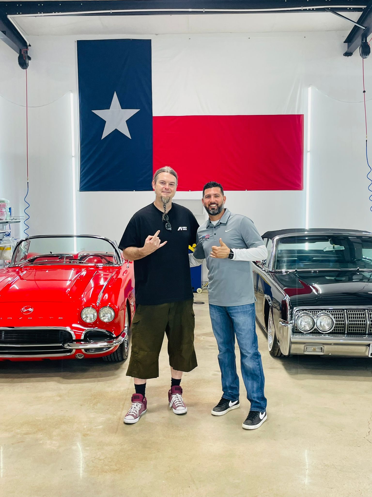 Two men are standing in front of a red car in a garage.