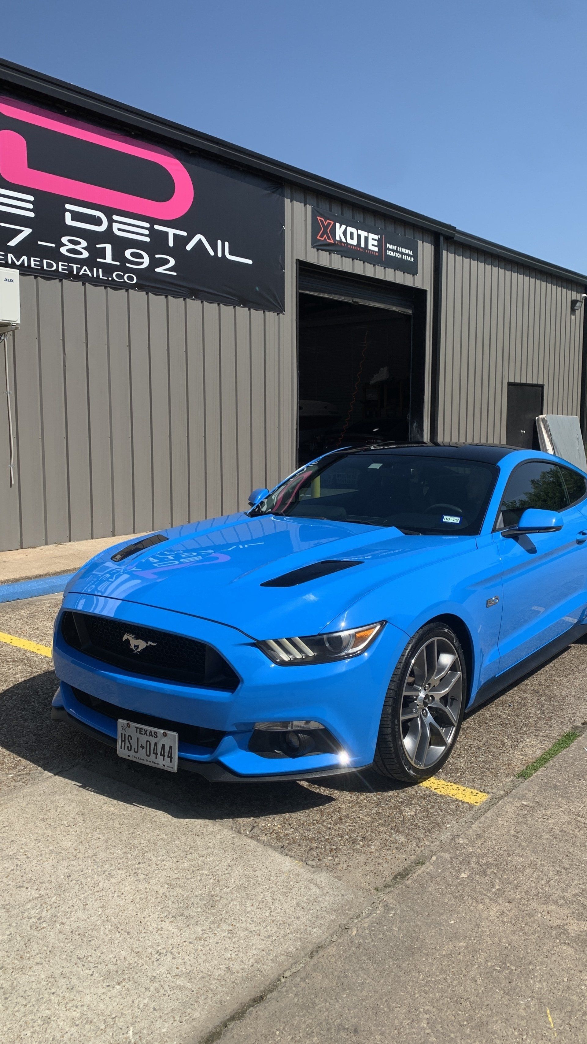 A blue mustang is parked in front of a building.
