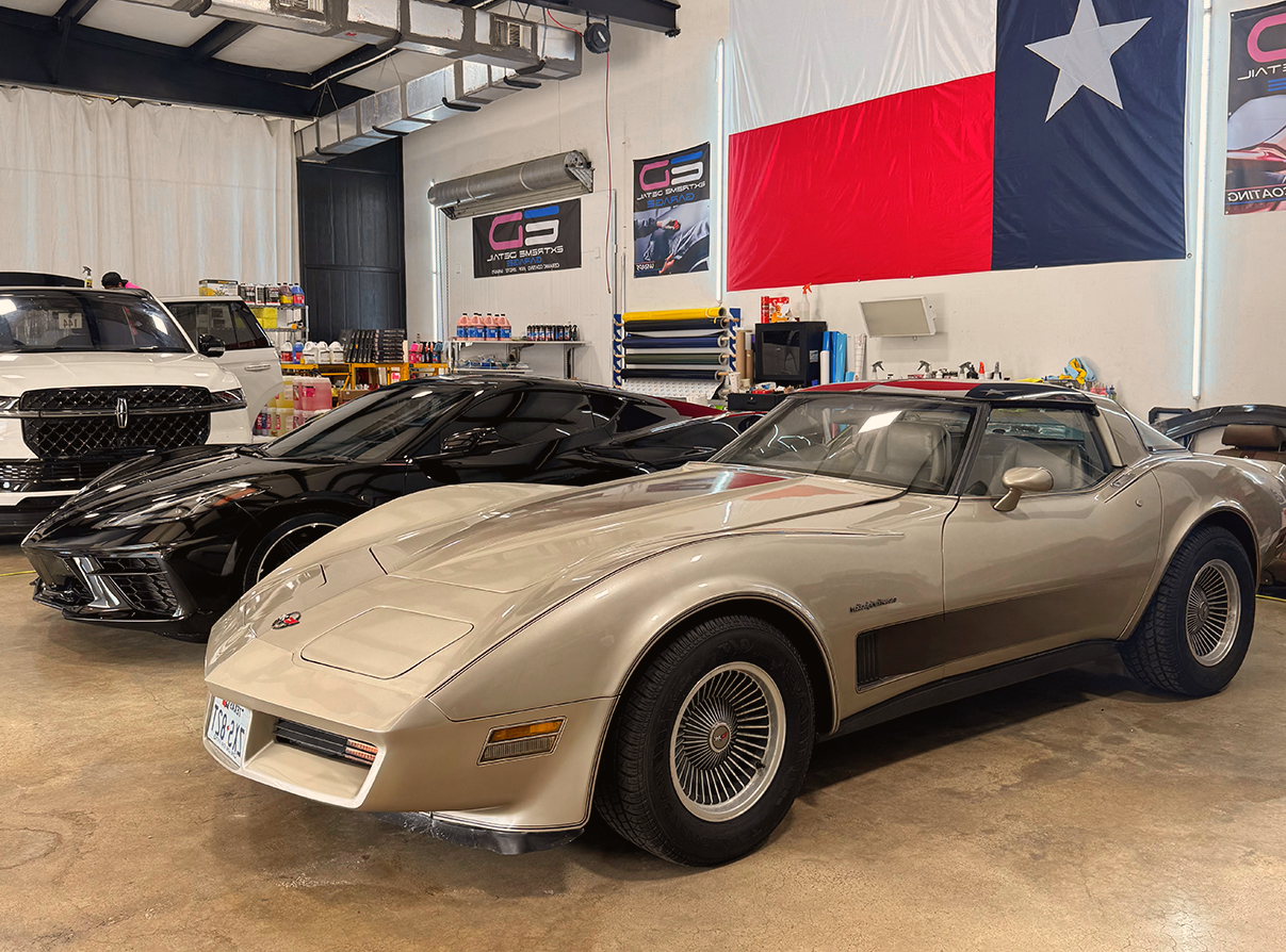 A silver corvette is parked next to a black corvette in a garage.