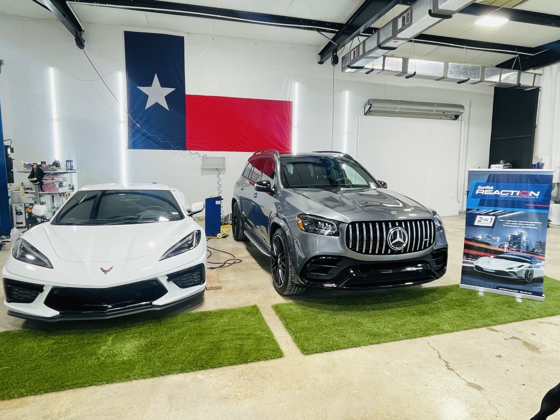 A white corvette and a gray suv are parked next to each other in a garage.