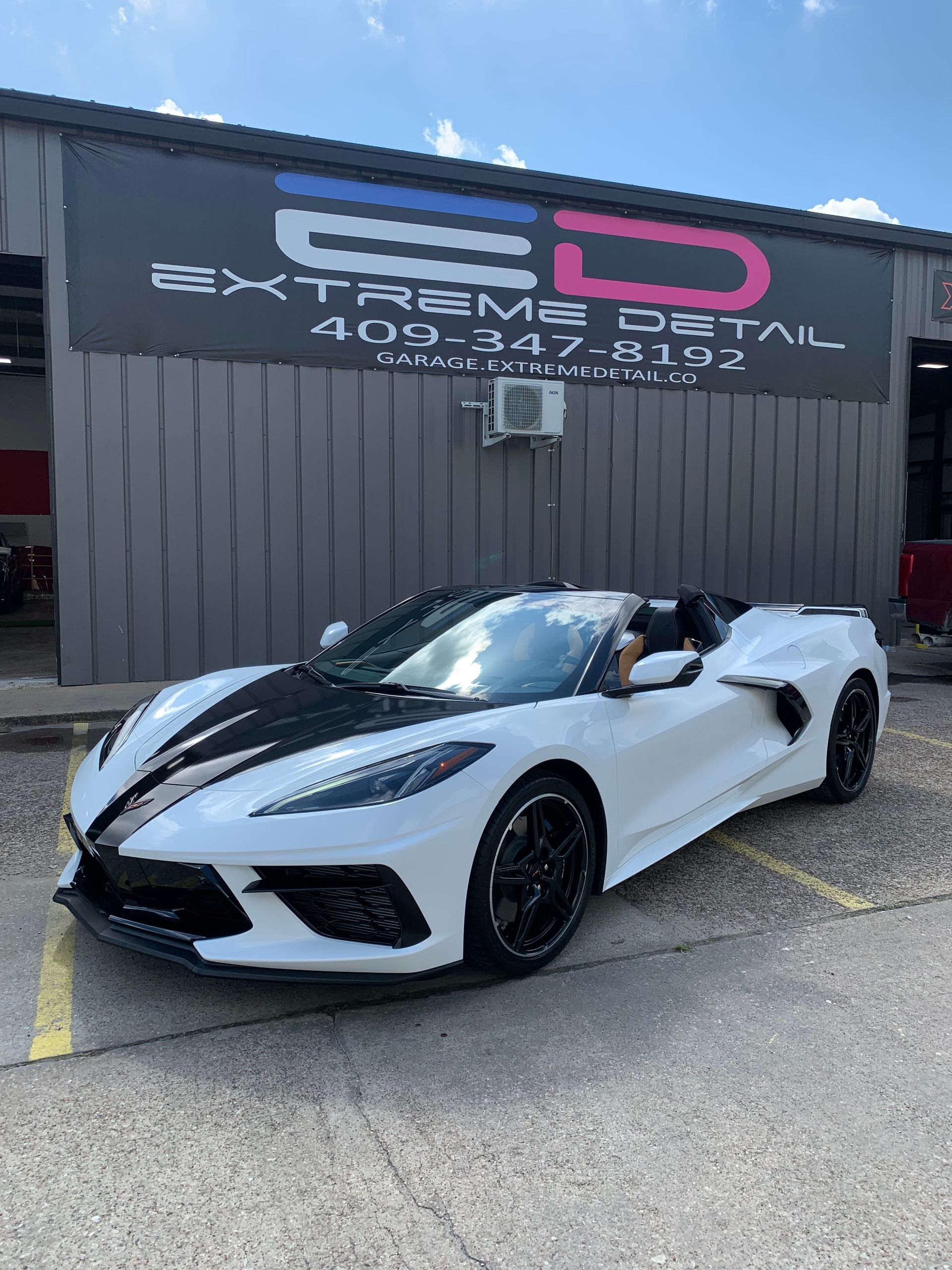 A white corvette convertible is parked in front of a building.
