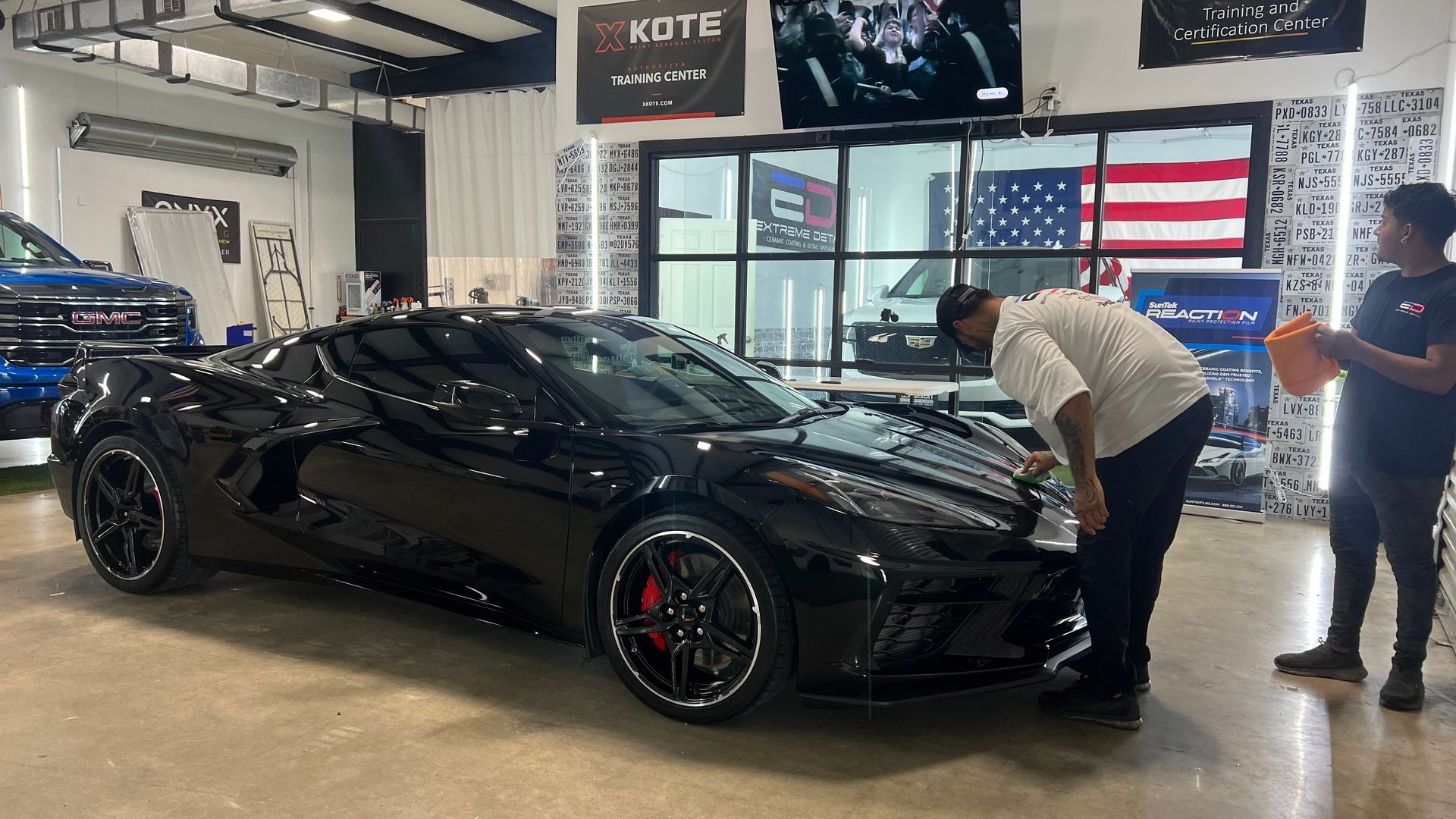 Two men are standing next to a black sports car in a garage.