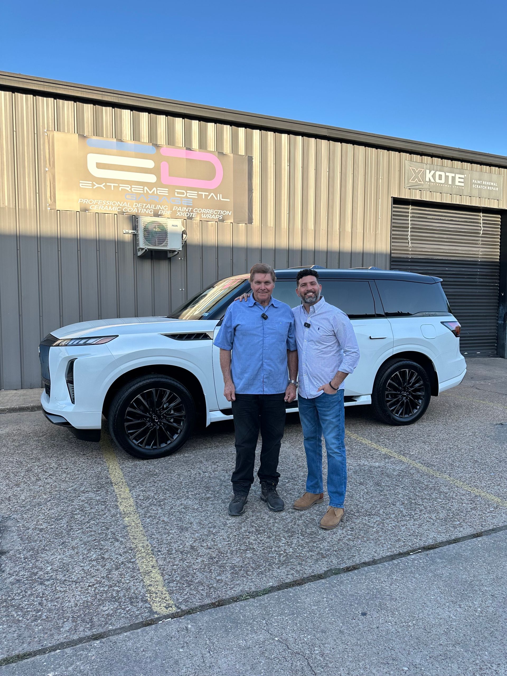 Two men are standing next to a white suv in front of a building.
