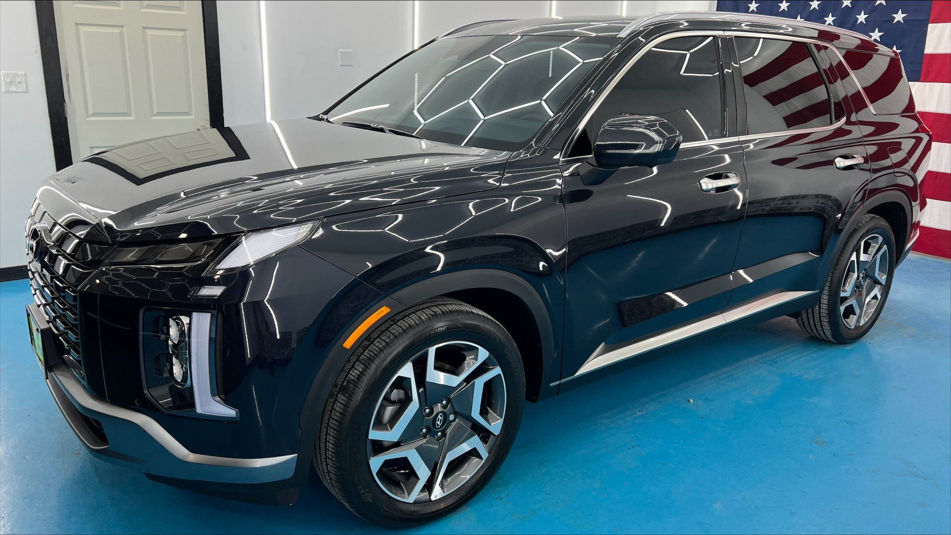 A black hyundai palisade is parked in front of an american flag.