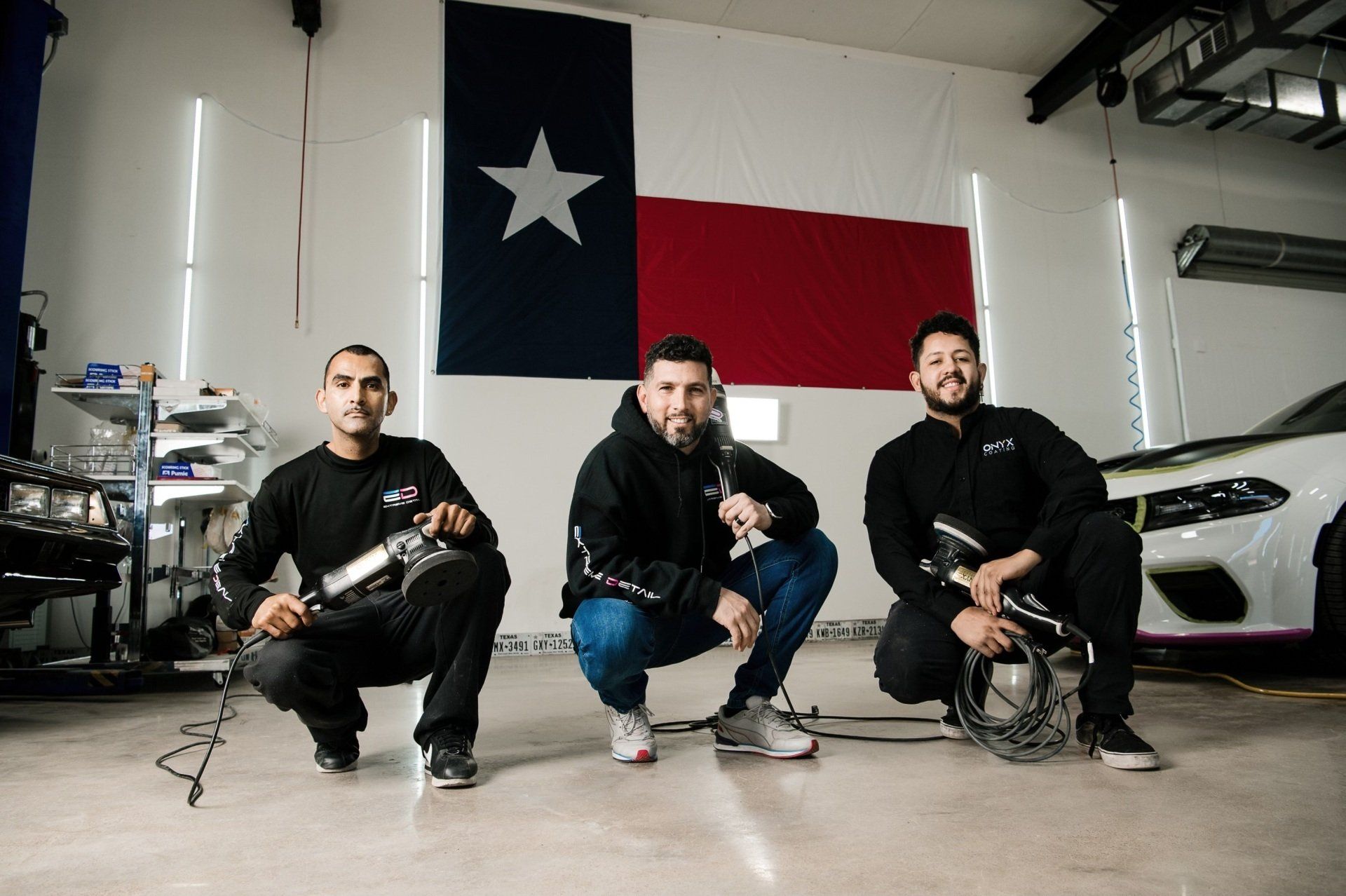 Three men are kneeling down in front of a texas flag in a garage.