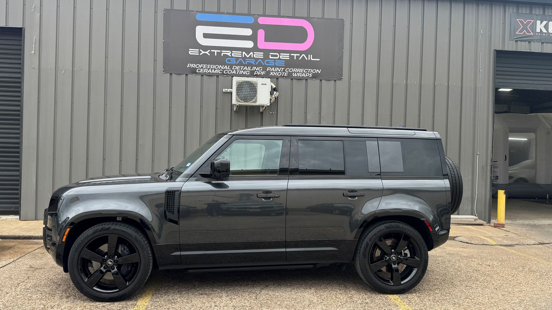 A black land rover defender is parked in front of a building.