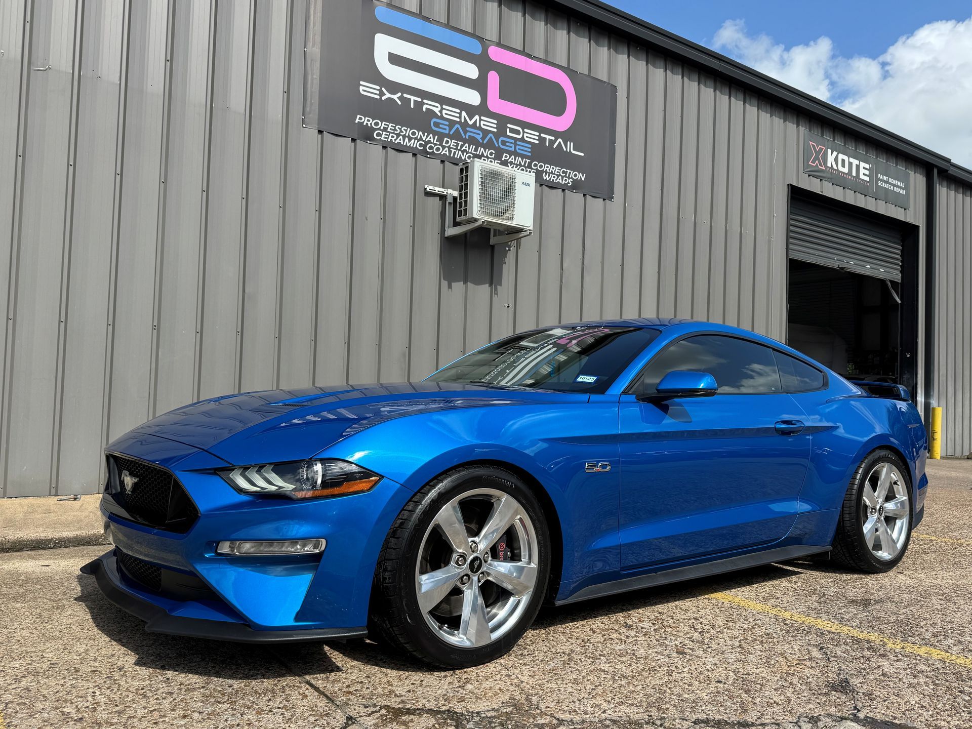 A blue ford mustang is parked in front of a building.