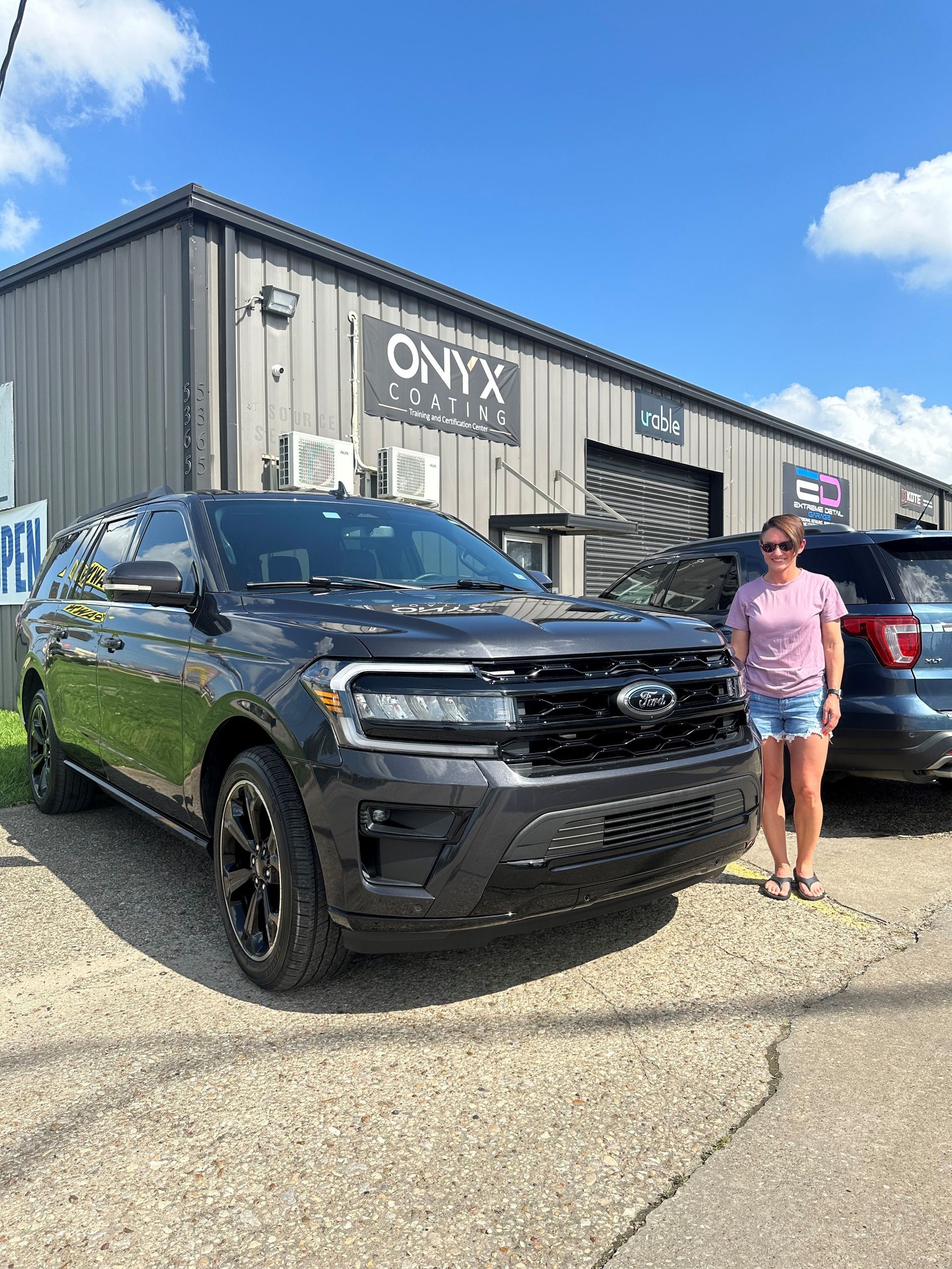 A woman is standing next to a black ford expedition.