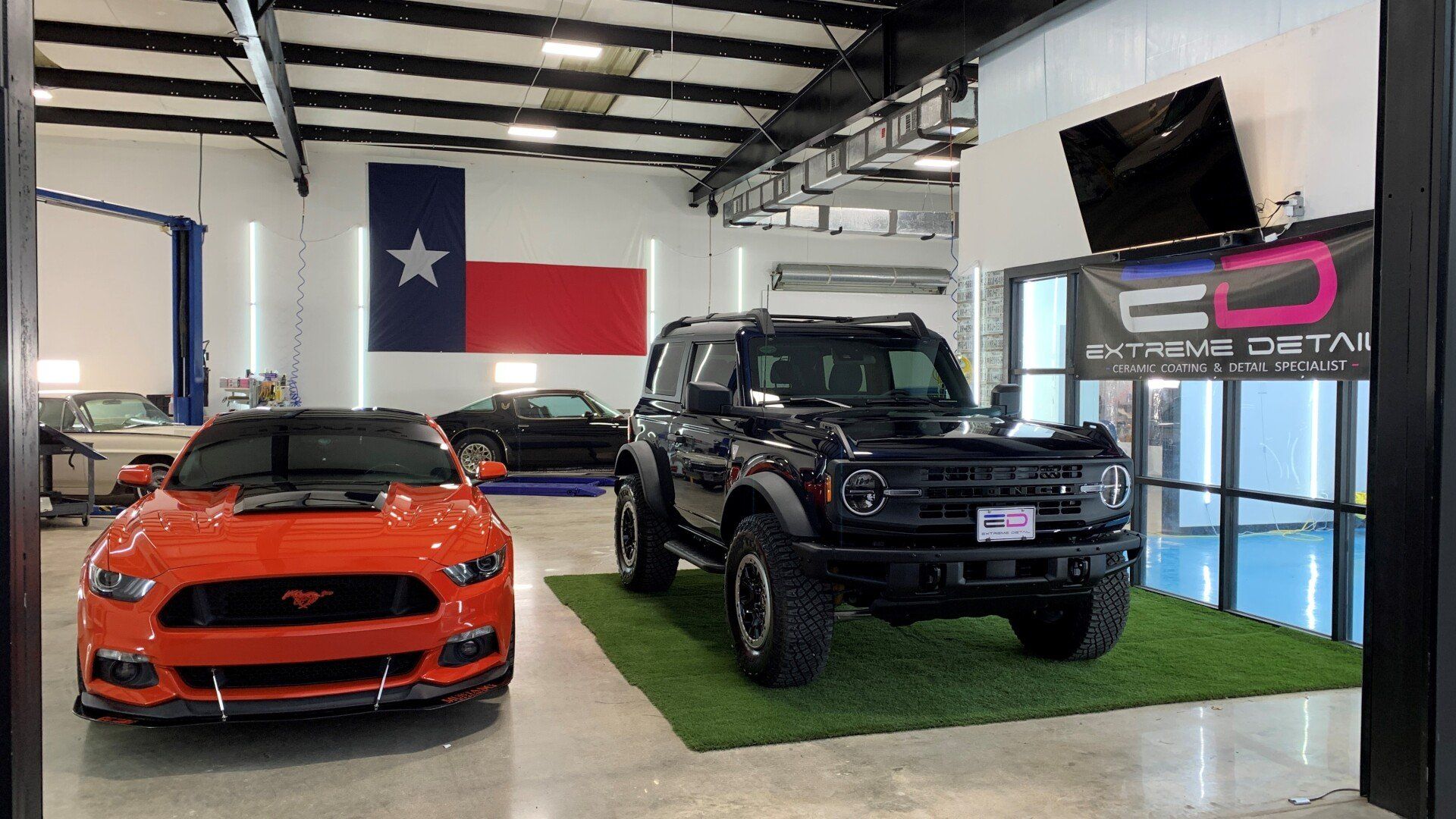 Two cars are parked in a garage with a texas flag on the wall.