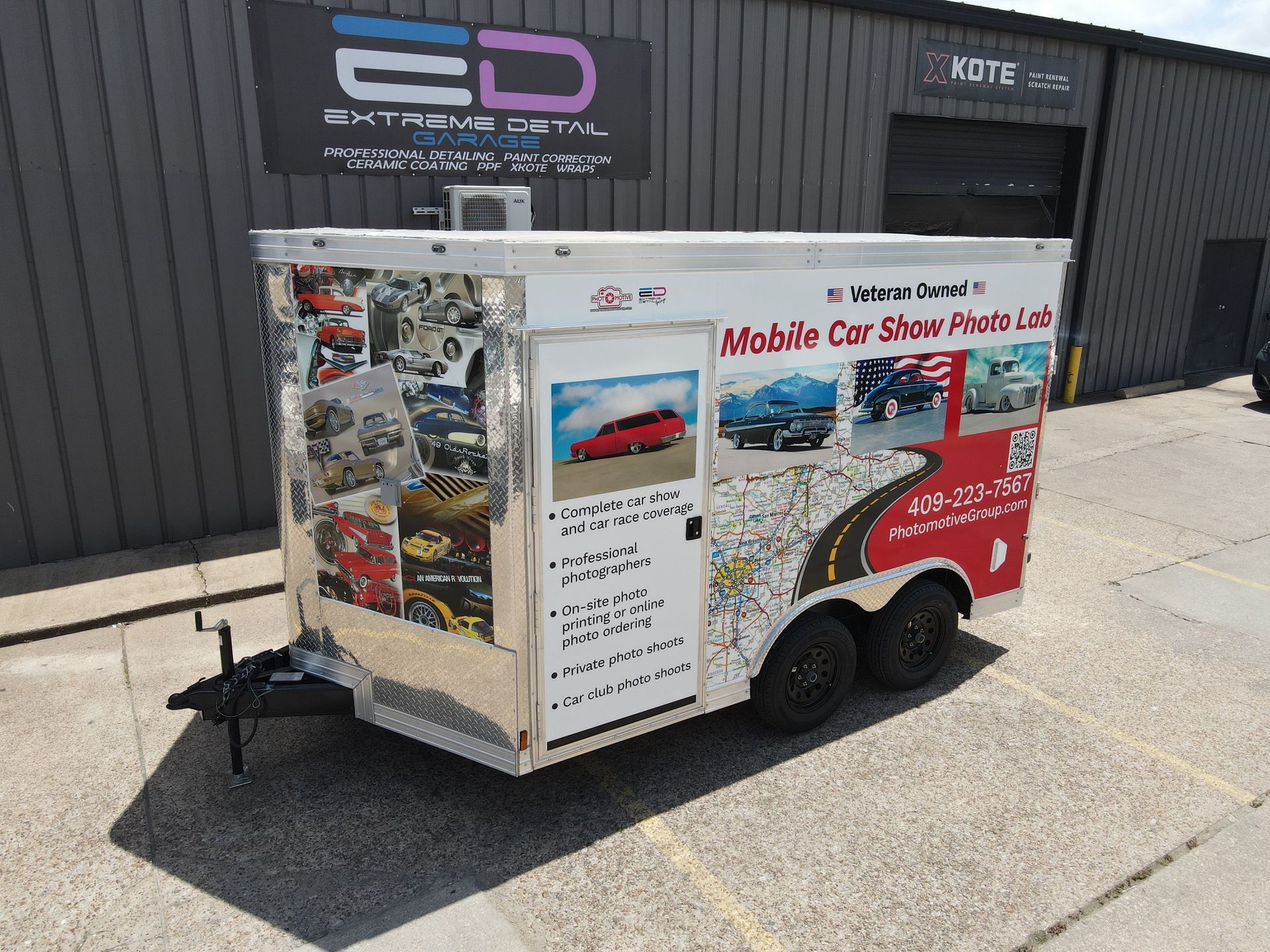 A mobile car show trailer is parked in front of a building.