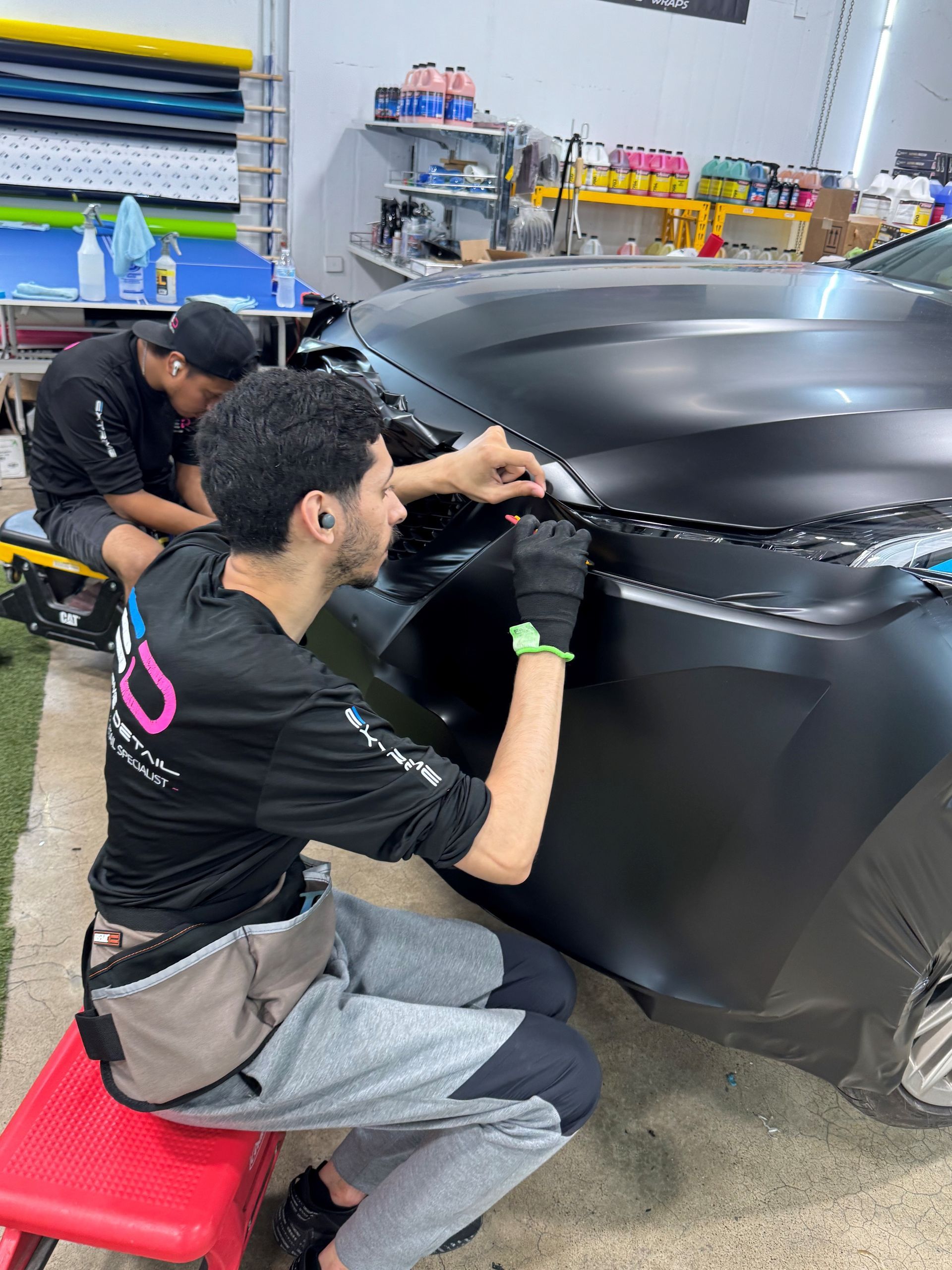 Two men are wrapping a black car in a garage.