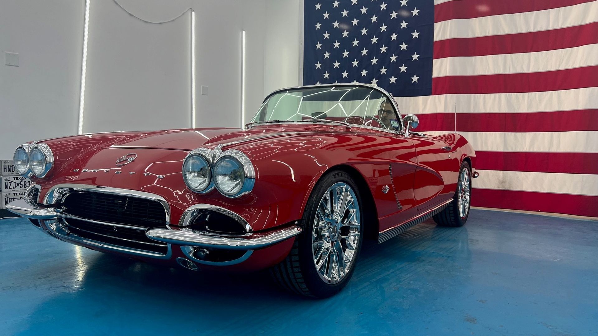 A red corvette convertible is parked in front of an american flag.